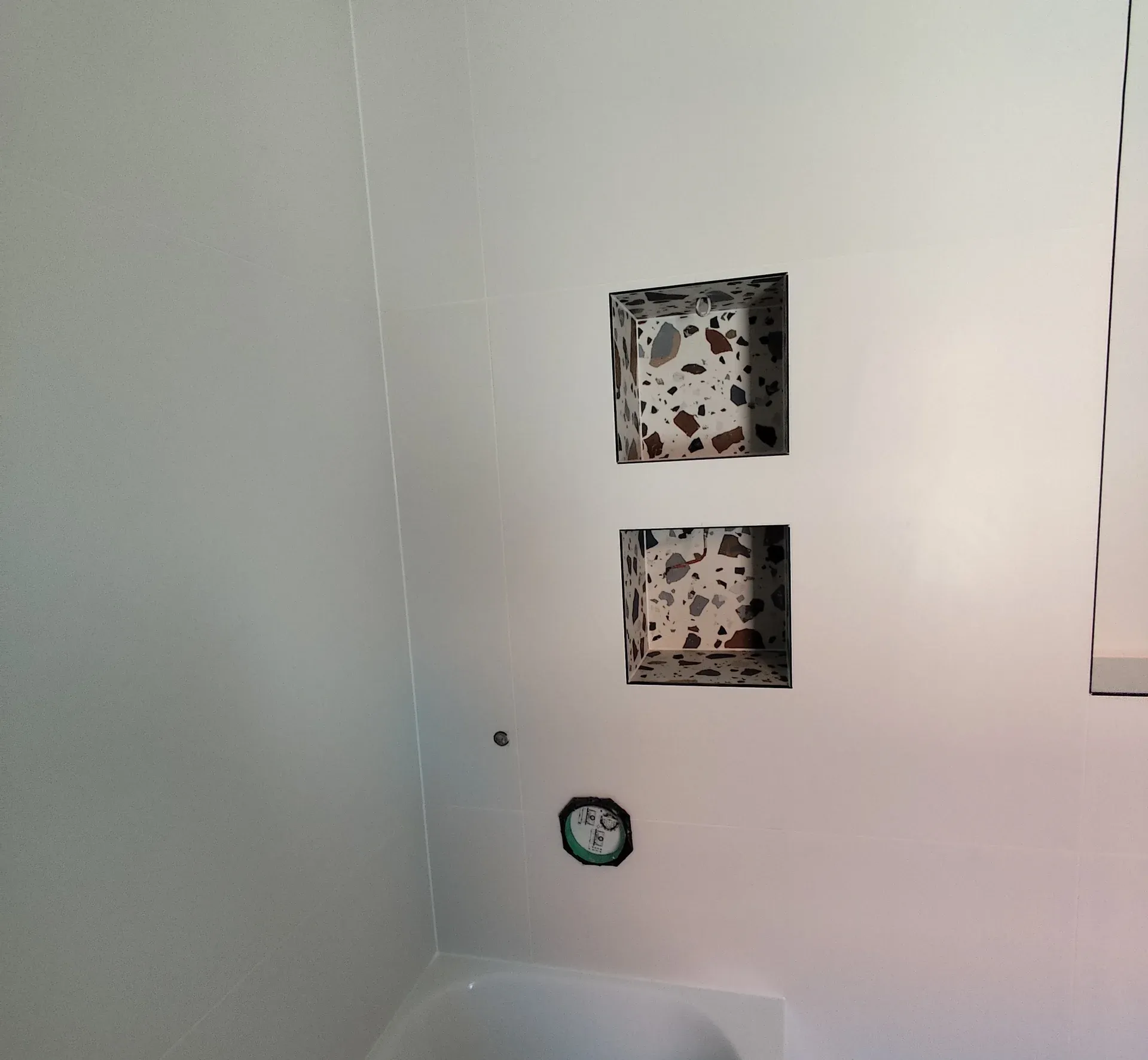 Fehér fürdőszobafal két beépített fülkével, terrazzo mintás belső burkolattal