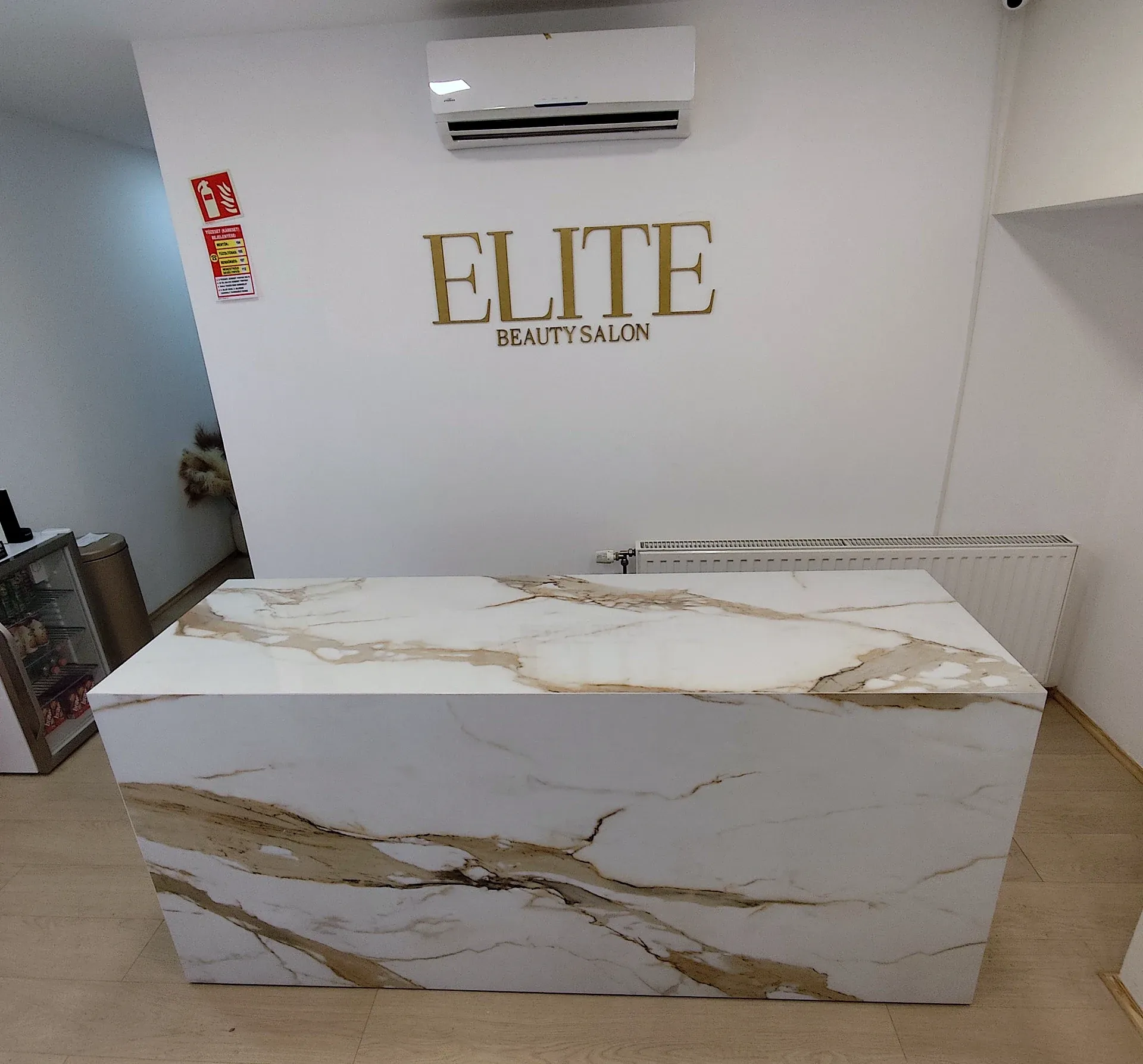 A kész recepciós pult az Elite Beauty szalon terében, szemből, az arany falifelirat alatt